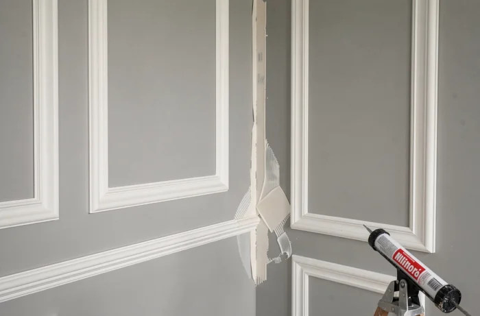 Pose de moulures décoratives collées en panneau rectangulaire sur un mur lisse gris clair dans un salon