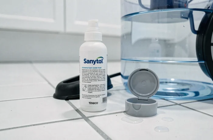 Flacon de Sanytol mousse posé à côté du réservoir d'eau d'un aspirateur laveur Tineco sur carrelage blanc